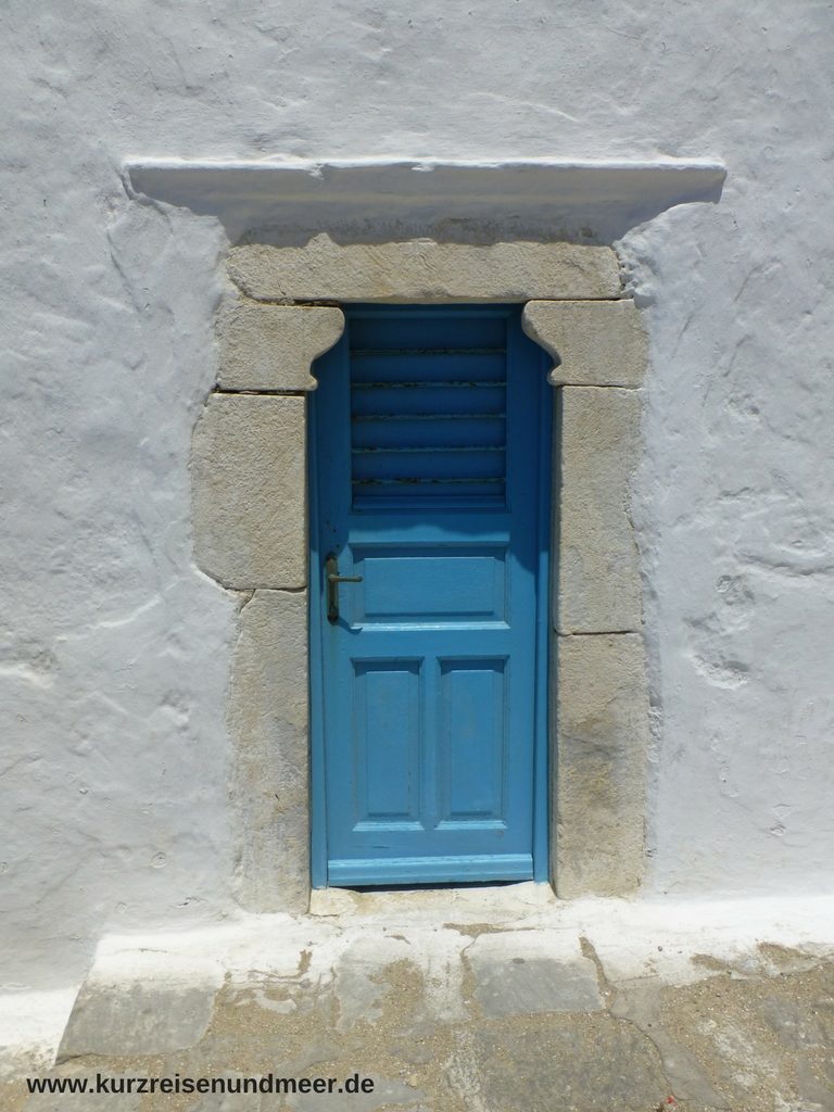 Das Bild zeigt eine blaue Tür in einer weißen Mauer.