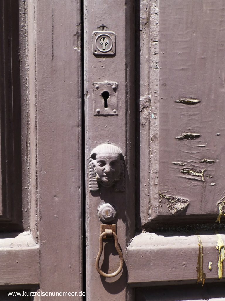 Das Bild zeigt eine alte Tür und über dem Schlüsselloch befindet sich zur Verzierung ein Kopf mit einem typischen ägyptischen Kopftuch. (Beitrag zur Foto-Blogparade)