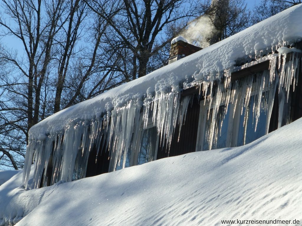 Das Bild zeigt ein Haus, an dessen Dachrinne lange Eiszapfen hängen